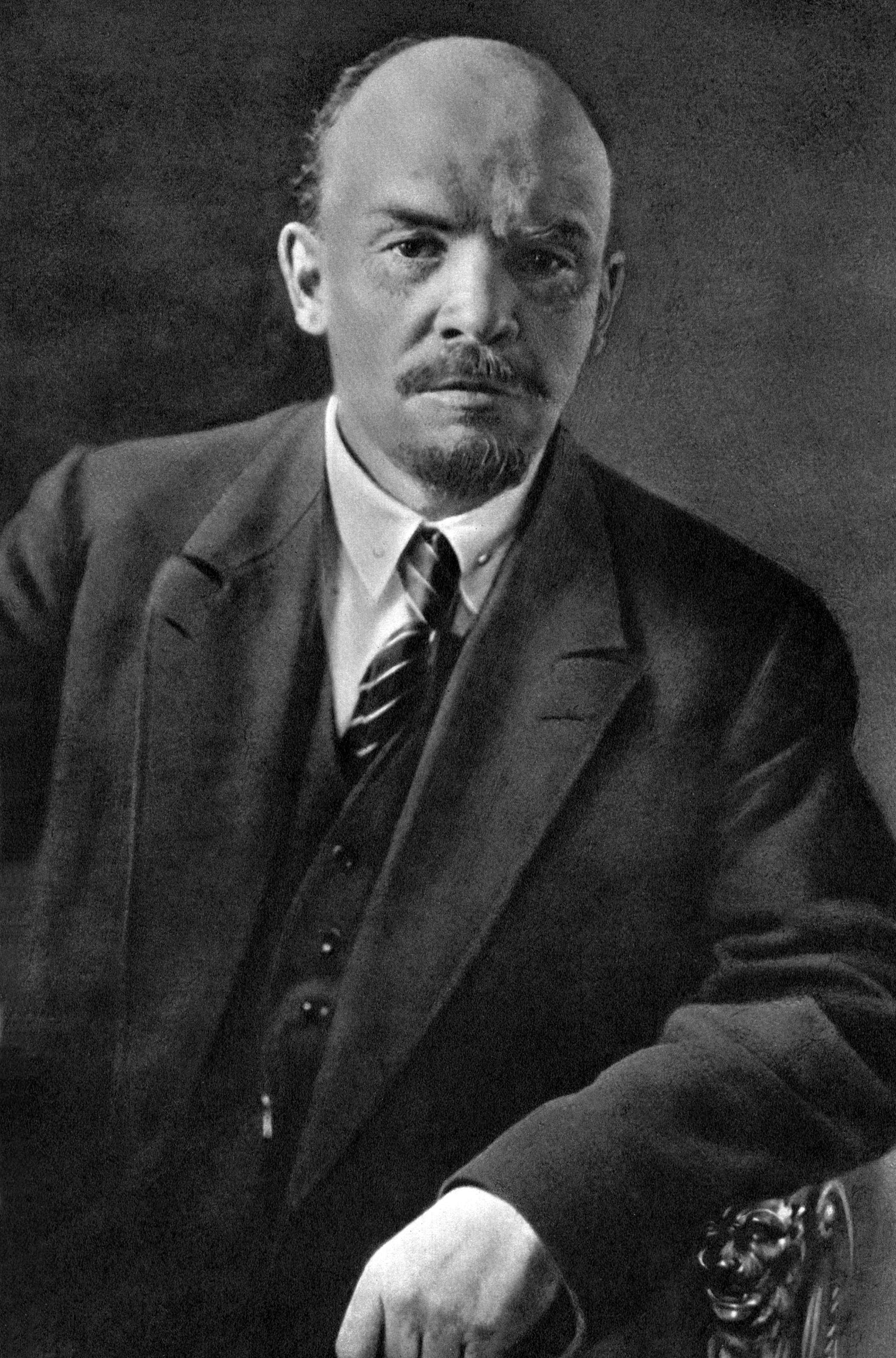 Photographie en noir et blanc de Vladimir Lénine en 1920. Homme d'âge mûr, crâne dégarni, légère barbiche, regard intense, costume sombre.