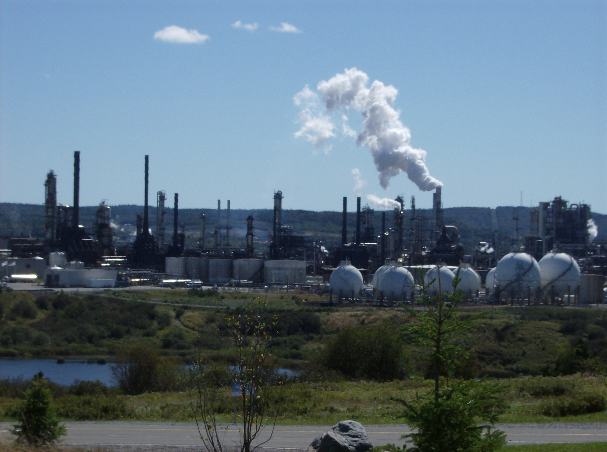 Photo de la raffinerie Irving Oil à Saint John (Nouveau-Brunswick, Canada). Vue d'ensemble du complexe industriel avec ses tours de distillation cylindriques, ses cheminées et son réseau de tuyaux.